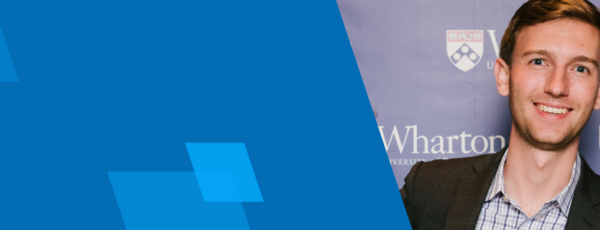 Mitch Gainer standing in front of a Wharton backdrop. He has short, brown hair and is wearing a black blazer over a blue shirt.