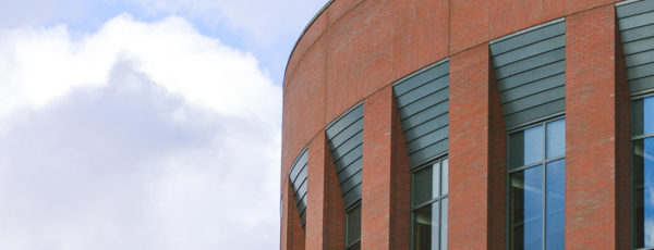The top left corner of Huntsman Hall. There are four large windows reflecting the dim blue of the cloudy sky.